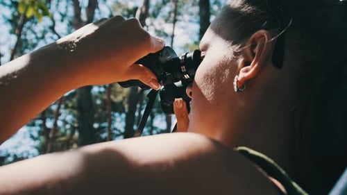 Woman Looks Through Binoculars on a Chaise Longue in a Forest Near Camping
