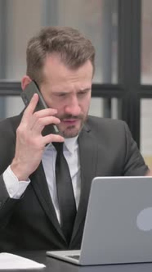 Serious Man Talking on Phone While Working on Laptop
