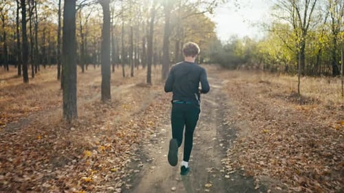 Rear View of a Brunette Man with Curly Hair in a Black Sports Uniform Runs Along an Earthen Path and