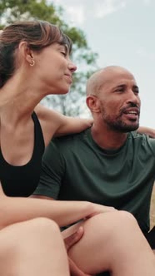 Side view of young athletic couple relaxing in the park in summer sitting on the grass