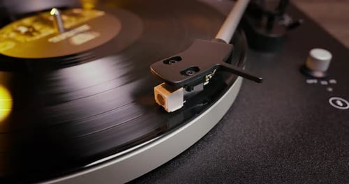 Detailed close-up of a turntable tonearm with white cartridge headshell, positioned over a black