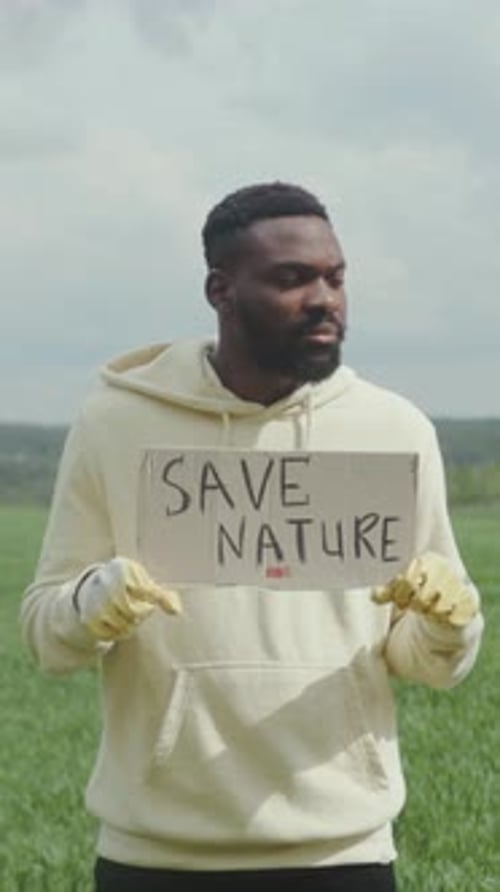 A Man Holds a Colorful Sign Promoting Nature Conservation in a Vibrant Green Field