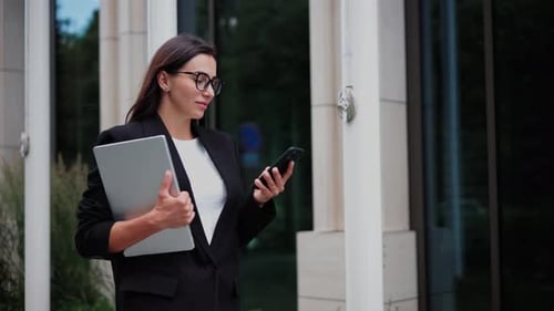 Business Woman Using Phone and Holding Laptop Outdoors