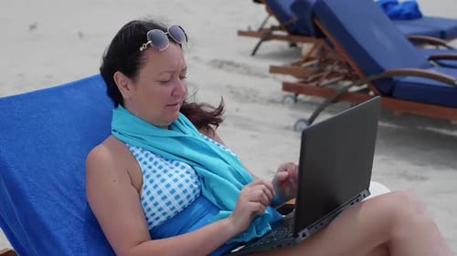 Freelancer arbeitet am Laptop und entspannt auf dem Liegestuhl am Strand