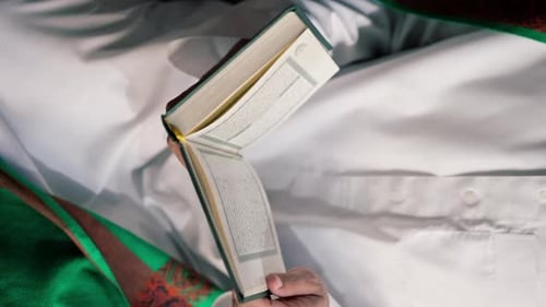 Nahaufnahme der Hände eines Muslims, der auf seinen Knien sitzt und in der Moschee mit dem Heiligen Koran betet