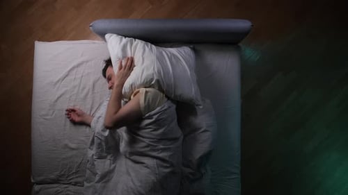 Restless Man Trying to Sleep Covering Ears with Pillow