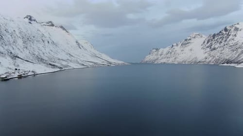 Drone view in Tromso area in winter flying over a blue fjord surrounded by white snowy mountains in