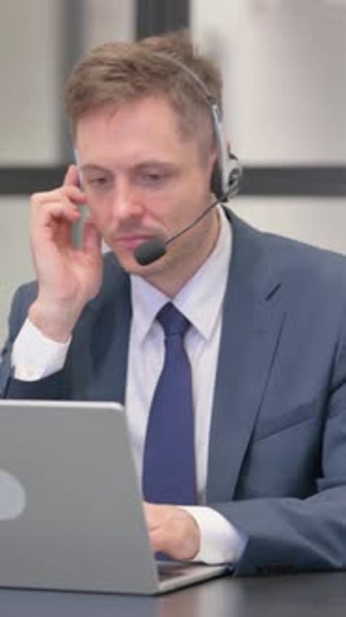 Man in Suit Using Laptop with Headset at Desk