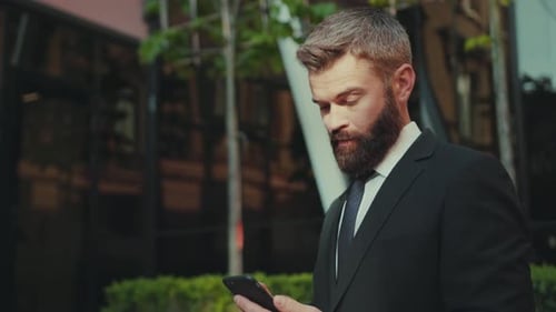 Successful Business Man Uses Smartphone Stand on Big City Business District Camera Moving Street