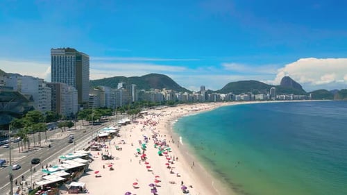 Uma vista panorâmica da praia de Copacabana, no Rio de Janeiro, com pessoas na areia, águas azuis claras e