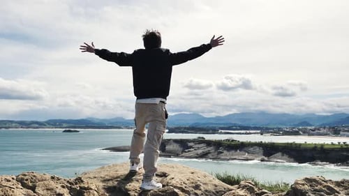 Young person raising arms on top of a mountain in front of the ocean-Freedom