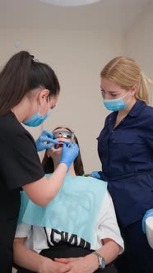 Female Dentist with Assistant Does Out Teeth Treatment Patient in Dental Clinic