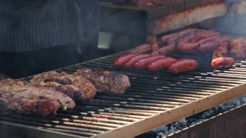 Nahaufnahme des Grillens von Würstchen und Rindfleisch auf einem Außengrill im Sommer.