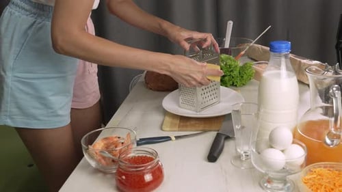 Hands of young European woman grate cheese with cheese grater, shredding parmesan to make pasta