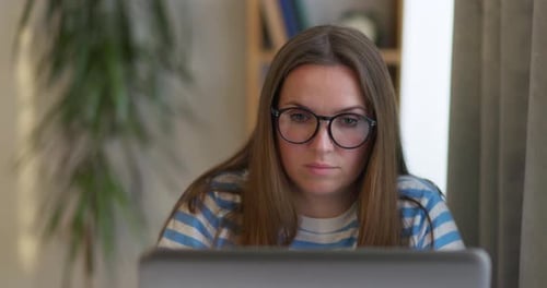A Thoughtful Woman in Glasses Working on a Laptop Computer