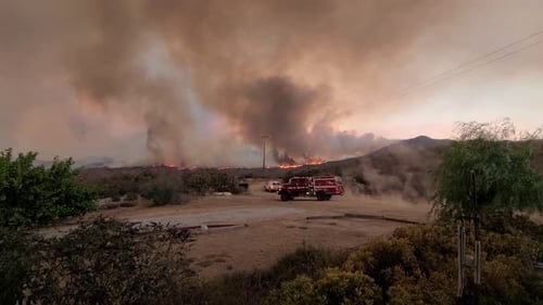 fire truck arrives in an area near a fire with a distant view of the burning and heavily smoking fir