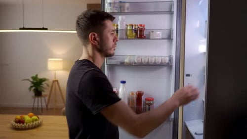 Man Opens Refrigerator Door and Takes Out Greens