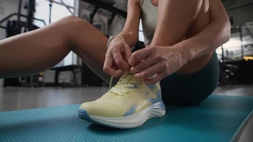 Unrecognizable Sportswoman Tying Shoelaces on Sneakers in Gym