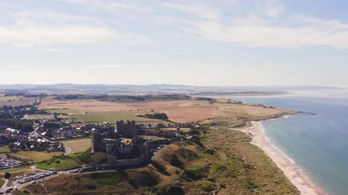 Drone shot pulls back to reveal a stunning ancient castle perched high on a hill by the sea on a sum
