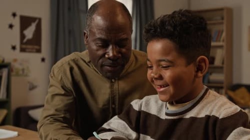 Black Grandfather and Grandson Laughing during Handwriting Practice