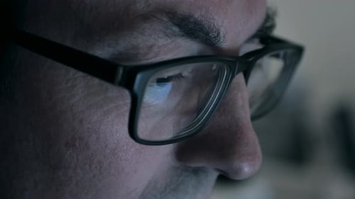 Man looking at screen with glasses. Close up, reflection of screen in glasses