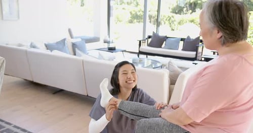 Smiling Caregiver Assists Senior Woman with Leg Exercise