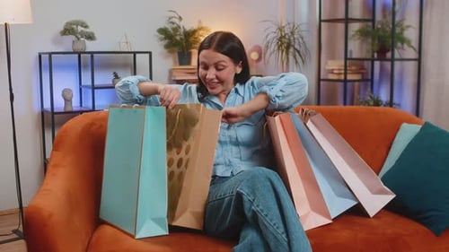 Glückliche junge kaukasische Shopaholic-Frau mit Einkaufstaschen, die zu Hause auf dem Sofa im Wohnzimmer sitzt