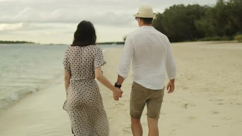 Young Couple Holding Hands and Walking Down the Beach Close to The
