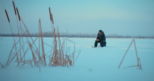 Ice Fisher Catching Fish in Frozen River in Sunrise or Sunset in Winter Ice Fishing Prores