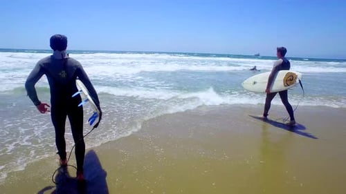 Two Young Men Carry Surfboards on Sunny Beach