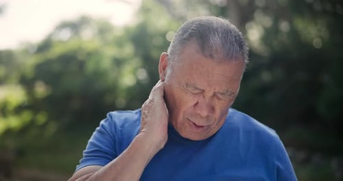 Mature Man Rubbing Neck in Outdoor Setting
