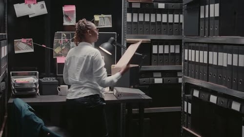 Woman Analyzes Investigation Paperwork in Cramped Office