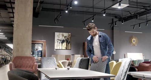 Male Consumer Choosing Furniture in Shopping Mall Looking at Table Shocked By Price