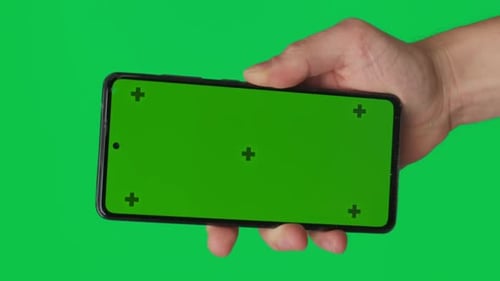 Male Hand Holding a Smartphone with Vertical Green Chroma Key Screen Isolated on Green Background