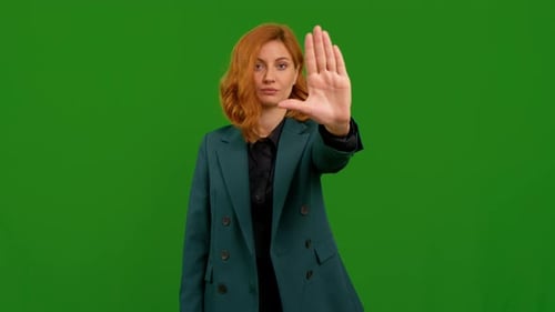 Pretty woman on green screen chroma key doing stop sign with left hand over isolated background.