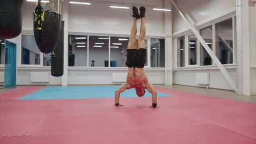 Bodybuilder with a Naked Torso Trains in a Sports Club and Pushes Up From the Floor While Standing