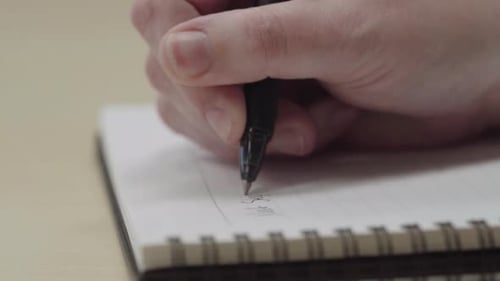 Close up of anonymous person's hands writing on a notebook with a pen in slow motion