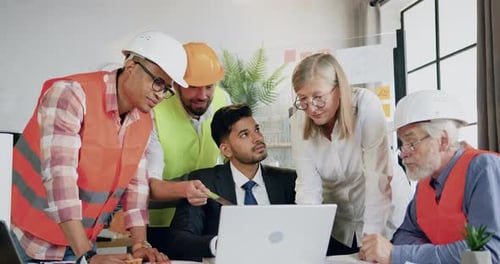 Team architects browsing building project on laptop together with confident skilled bearded head man