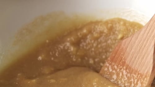 Makro-Nahaufnahme eines Holzspatels, der flüssigen Teig in einer Schüssel mischt