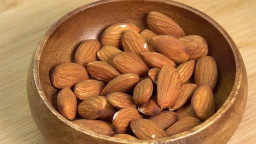 Hand takes Almond nut from wooden bowl rotate on wooden background close up. Product rich
