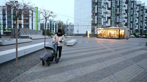 Woman Walks with Stroller Through Modern Urban Area During Early Morning Hours in a Quiet