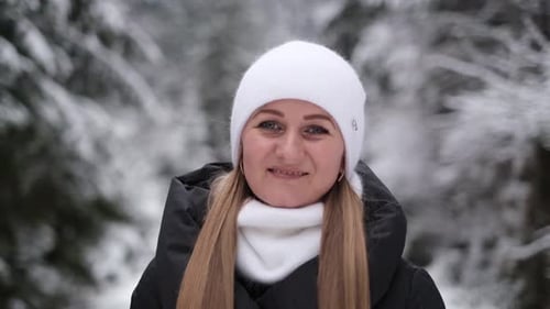 Portrait of a Beautiful Girl in a White Hat Against a Background of Snowy Fir Trees