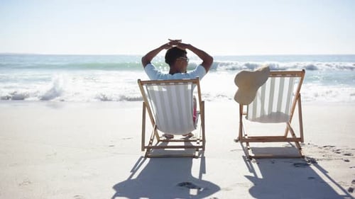A young man relaxes on beach chair facing ocean, copy space