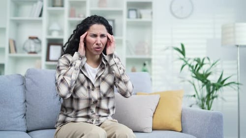 Woman with Headache Rubbing Temples on Couch