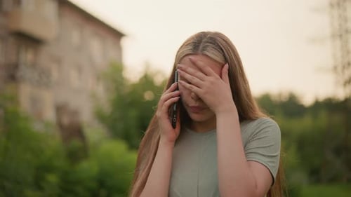 Erschöpfte Frau telefoniert im Freien mit Hand auf der Stirn