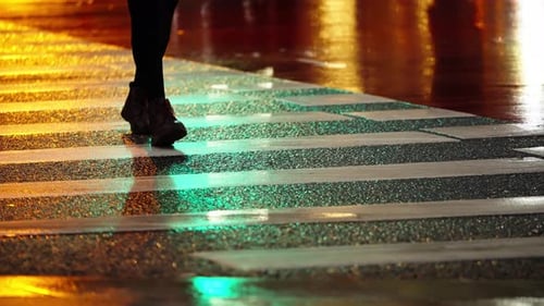 Lone Pedestrian in Dark Boots Crossing a Rainsoaked Zebra Crosswalk at Night Illuminated By Vibrant