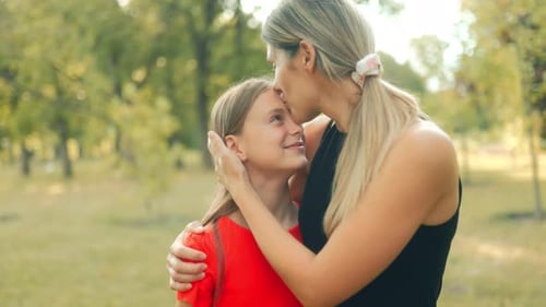 Mom Hugs Daughter in Warm Embrace Under Trees in Peaceful Green Park Setting