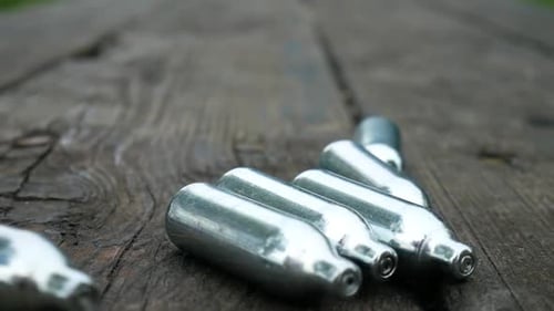 Vários cilindros metálicos de gás de óxido nitroso, droga recreativa em câmera lenta rolando em um par de madeira