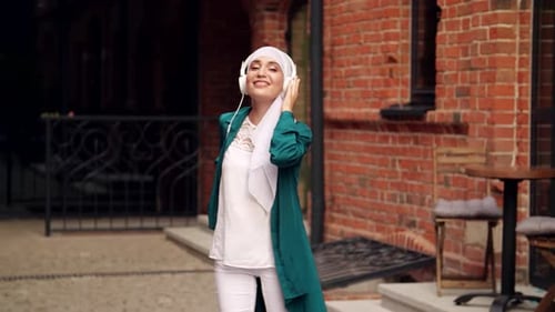 Frau aus dem Nahen Osten im Hijab hört Musik mit Kopfhörern und tanzt