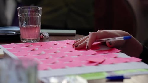 Eine Hand, die während einer Brainstorming-Sitzung mit einem Getränk in der Nähe Notizen auf einen Tisch legt